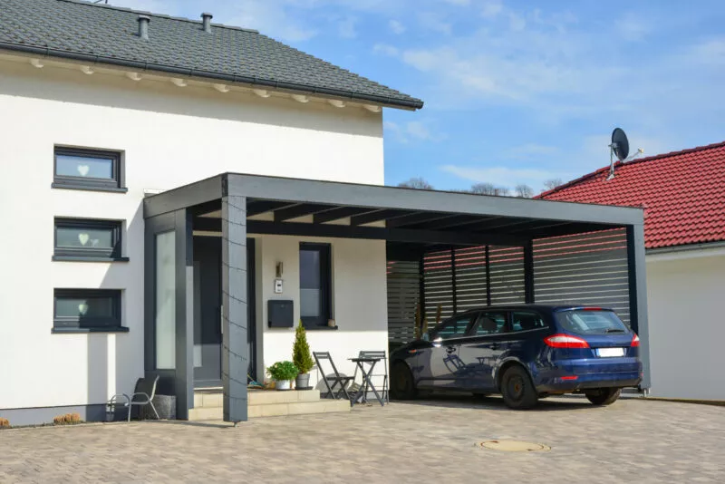 Moderner Carport aus lasiertem/lackiertem Holz im Einfahrtsbereich eines Wohnhauses